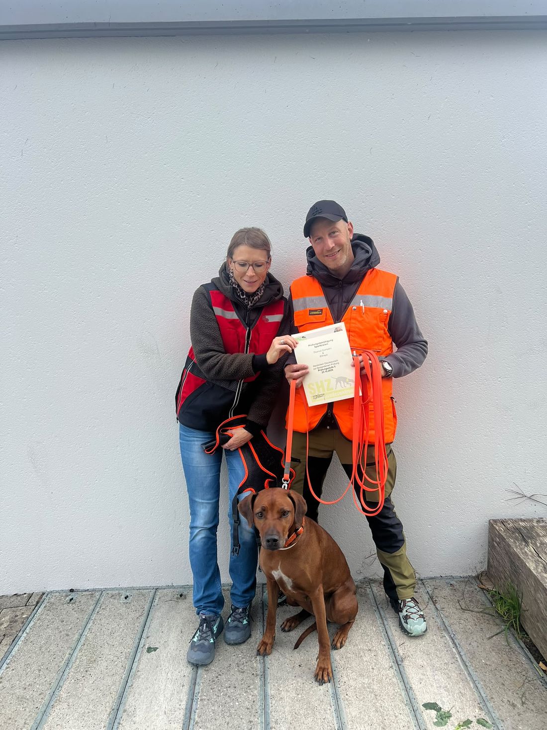 Karin und Thomas in Warnwesten mit ihrem Ridgeback und einer Urkunde
